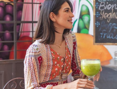 Woman holding a refreshing green juice in a lively café setting with colorful decor.