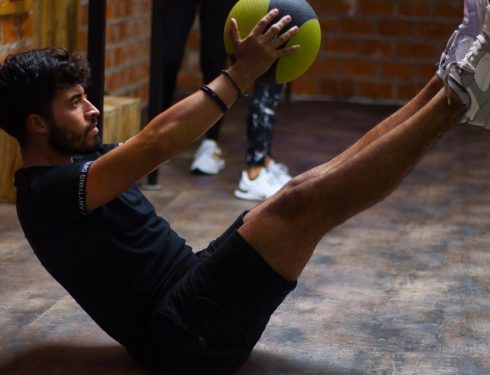 Focused man performing core exercises with a medicine ball in an indoor gym highlighting fitness and strength.